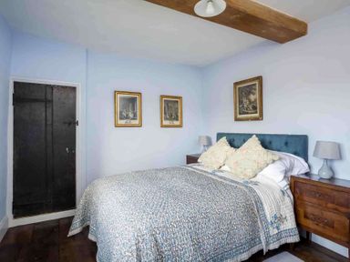 A bedroom with a bed covered by a patterned quilt and two pillows and wooden nightstands with lamps at Shenley Broadwell