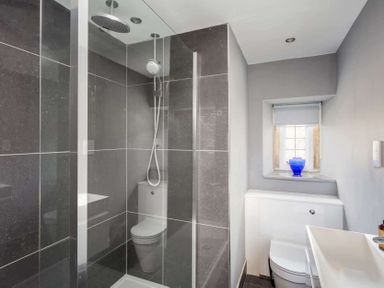 A bathroom with a glass shower enclosure a toilet a sink and a small window with a blue vase on the sill at Shenley in Broadwell