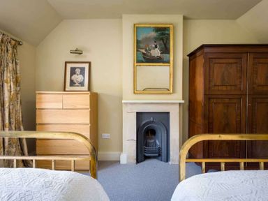 A bedroom with two brass beds a fireplace between a wooden dresser and a wooden wardrobe at Shenley in Broadwell
