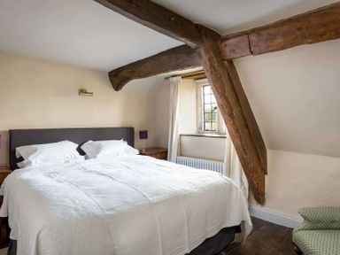 A bedroom with a double bed white bedding wooden beams and a window at Shenley Broadwell
