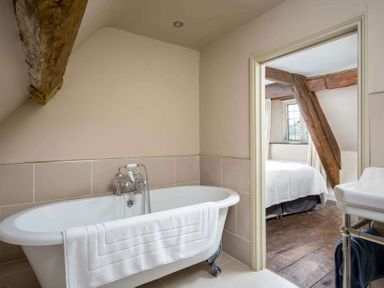 A bathroom with a white freestanding bathtub and towel and a view into a bedroom with wooden beams at Shenley in Broadwell