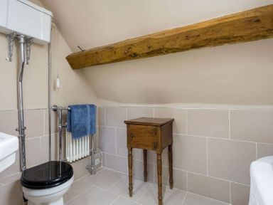 A bathroom with a toilet a radiator with a towel a wooden side table and a wooden beam on the ceiling at Shenley in Broadwell