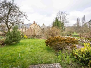 A garden with trees shrubs and a stone wall with houses in the background at Shenley in Broadwell