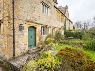 Stone house with a green door and windows with leaded glass and a garden with bushes and a bench at Shenley in Broadwell