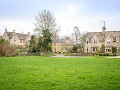 A green grassy field with three stone houses and leafless trees at Shenley in Broadwell