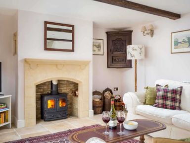 A living room with a fireplace wood burning stove sofa table with wine and glasses at Oyster Barn in Naunton