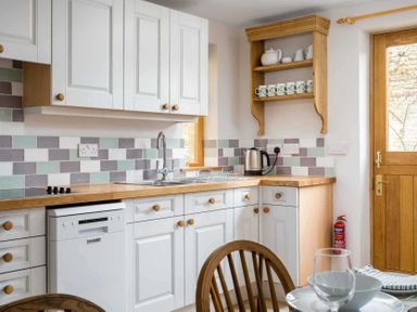 A kitchen with white cabinets a wooden countertop a stainless steel sink a kettle and cups on a wooden shelf at Oyster Barn in Naunton