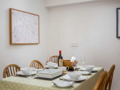 A dining table set with white bowls plates wine glasses and a bottle of wine with wooden chairs at Oyster Barn in Naunton