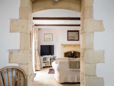 A living room with a sofa facing a fireplace and a television near a window at Oyster Barn in Naunton