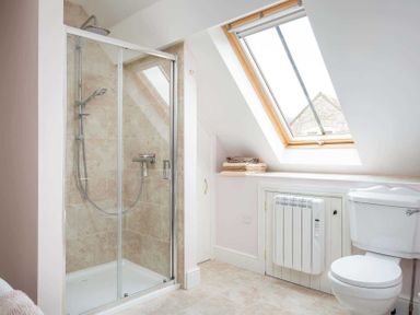 A bathroom with a shower enclosure toilet stacked towels under a skylight window and a wall-mounted heater at Oyster Barn in Naunton