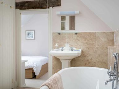 A bathroom with a clawfoot bathtub sink and a door opening to a bedroom at Oyster Barn in Naunton