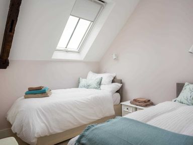 A bedroom with two single beds a skylight window and folded towels at Oyster Barn in Naunton