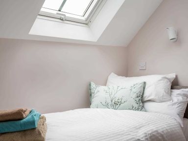 A small bedroom with a bed under a skylight window and folded towels at Oyster Barn in Naunton