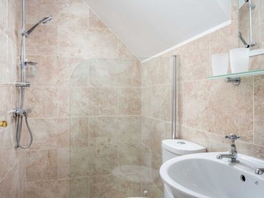 A bathroom with a shower area, toilet, sink, and a glass shelf with two glasses at Oyster Barn in Naunton