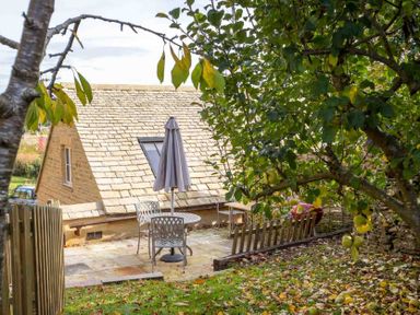 A garden area with a table and chairs under a closed umbrella near a stone building at Oyster Barn in Naunton