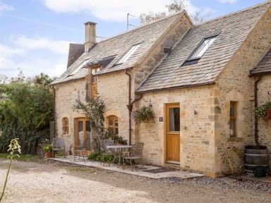 A stone house with wooden doors and windows and outdoor metal chairs and tables at Oyster Barn in Naunton