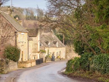 A narrow road curving past stone houses and trees at Oyster Barn in Naunton