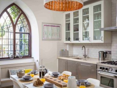 A kitchen with a dining table set with bowls orange juice and a coffee press near a window at Little Culver in Minchinhampton