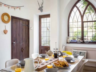 A dining area with a table set for breakfast next to arched windows and a wooden door at Little Culver in Minchinhampton