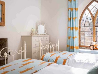 A bedroom with two white metal beds blue and orange fox patterned blankets a chest of drawers and a window with blue curtains with orange foxes at Little Culver Minchinhampton