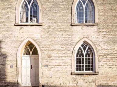 A stone wall with two arched windows and a white arched door at Little Culver in Minchinhampton