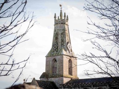 A clock tower on a stone building with bare tree branches in the foreground at Little Culver in Minchinhampton
