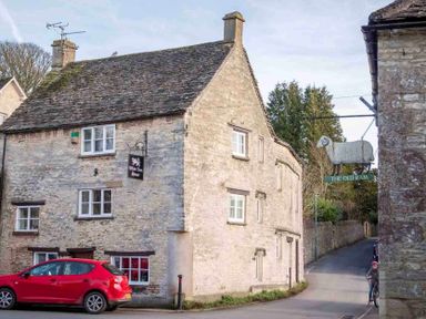 A stone building with signs reading White Lion House and The Old Ram with a red car parked in front and a person on a bicycle nearby