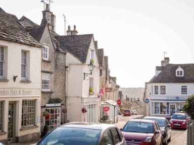 A street with parked cars and shops including a post office and a hair and beauty salon at Little Culver in Minchinhampton