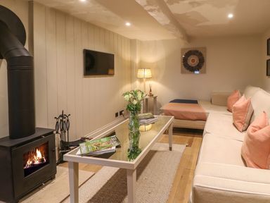 A sitting room with a sofa a glass coffee table a wood burning stove and a television at Spinners Cottage in Stow-on-the-Wold