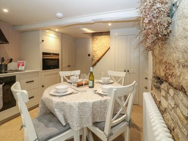 A kitchen dining area with a round table set for four beside stone walls at Spinners Cottage in Stow-on-the-Wold