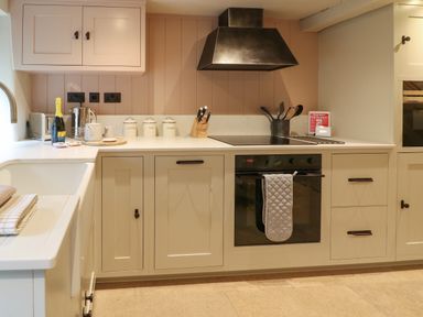 A kitchen with white cabinets a stove oven and countertop items at Spinners Cottage in Stow-on-the-Wold
