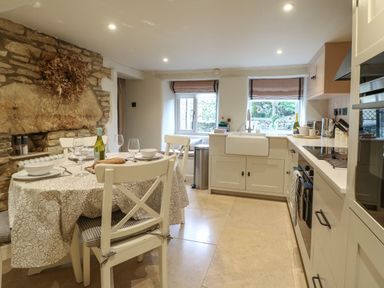 A kitchen with a dining table set with plates glasses and a bottle of wine next to a stone fireplace at Spinners Cottage in Stow-on-the-Wold