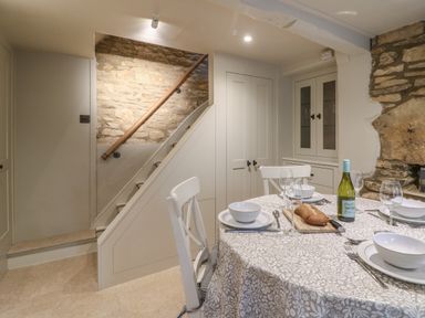 A dining area with a table set for four beside a staircase and stone walls at Spinners Cottage in Stow-on-the-Wold