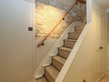 A staircase with carpet runners and a wooden handrail next to a stone wall and built-in cupboards at Spinners Cottage in Stow-on-the-Wold