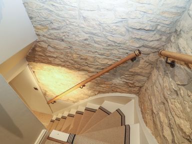 A staircase with carpeted steps and wooden handrails on stone walls at Spinners Cottage in Stow-on-the-Wold