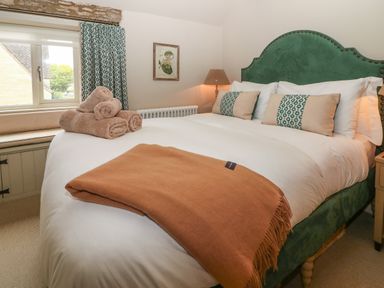 A bedroom with a green upholstered bed a white duvet and beige and green pillows at Spinners Cottage in Stow-on-the-Wold