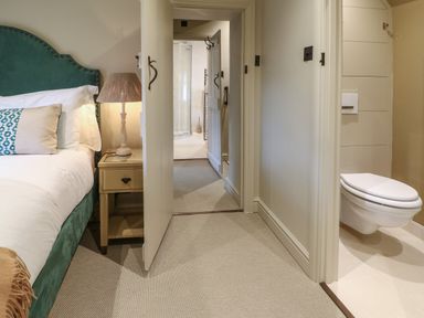 A bedroom with a bed and lamp next to an open door leading to a bathroom with a toilet at Spinners Cottage in Stow-on-the-Wold