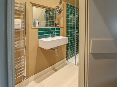 A bathroom with a wall mounted sink and green tile backsplash at Spinners Cottage in Stow-on-the-Wold