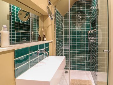 A bathroom with a sink countertop mirror and a shower area with green tiles at Spinners Cottage in Stow on the Wold