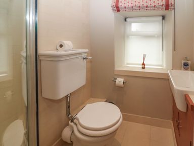 A bathroom with a toilet a window with blinds a small sink and a shower at Spinners Cottage in Stow-on-the-Wold