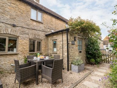 An outdoor stone patio with a table set for breakfast and four wicker chairs at Spinners Cottage in Stow-on-the-Wold