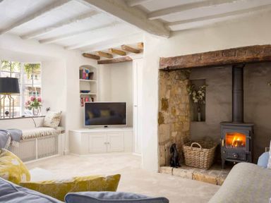 A living room with a wood burning stove books a TV and a window seat at Stanley Cottage in Chipping Campden