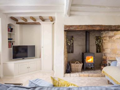 A living room with a wood burning stove fireplace a television and built in shelves at Stanley Cottage in Chipping Campden