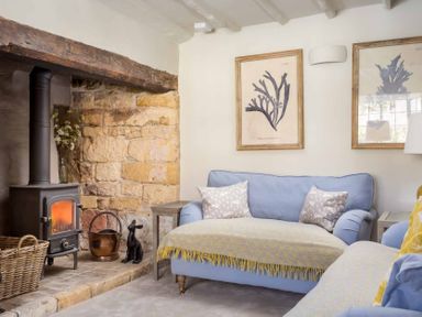 A living room with a wood burning stove stone wall and two blue sofas at Stanley Cottage in Chipping Campden