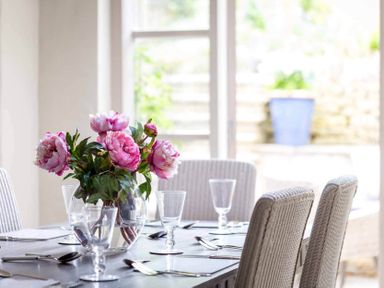 A dining table with glasses cutlery and a vase of pink flowers at Stanley Cottage in Chipping Campden