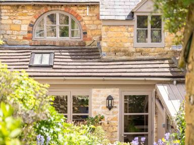 The exterior of a stone house with multiple windows and a garden in front at Stanley Cottage in Chipping Campden
