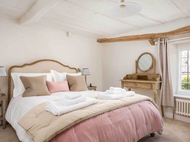 A bedroom with a bed with pillows and folded towels and a wooden dressing table by a window at Stanley Cottage in Chipping Campden