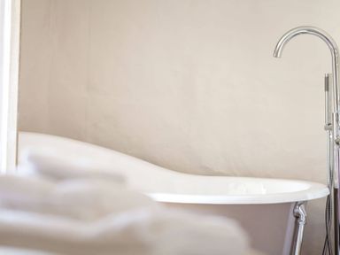 A white freestanding bathtub with a chrome faucet and blurred white towels in the foreground at Stanley Cottage in Chipping Campden