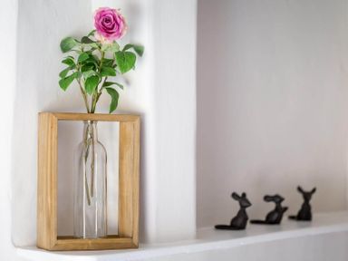 A pink rose in a glass bottle inside a wooden frame with three small black mouse figurines on a white shelf at Stanley Cottage in Chipping Campden