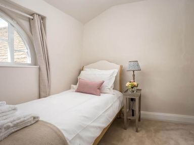 A bedroom with a single bed pillows and a bedside table with a lamp and flowers at Stanley Cottage in Chipping Campden